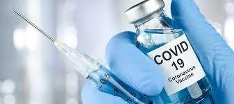 Gloved hand holding a syringe and a vial of COVID 19 Vaccine